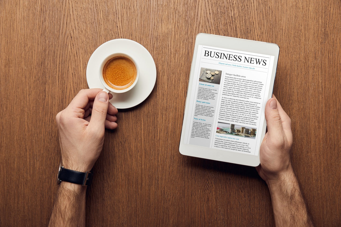 A man is seated at a table, holding a coffee cup in one hand and tablet with Business News headline in the other